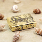 Gold Zippo lighter with an Avengers engraving on a sandy surface, inscribed: 'Love you three thousand times', surrounded by seashells.