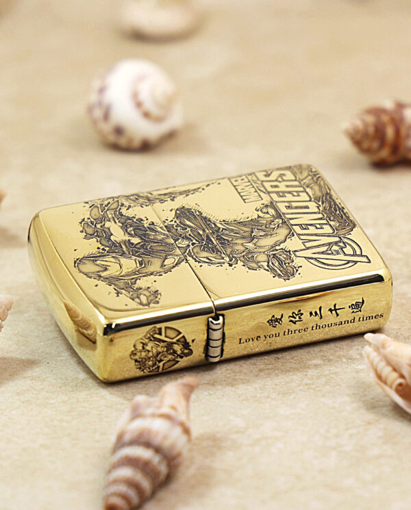 KZ241-04 Gold Zippo lighter with an Avengers engraving on a sandy surface, inscribed: 'Love you three thousand times', surrounded by seashells.