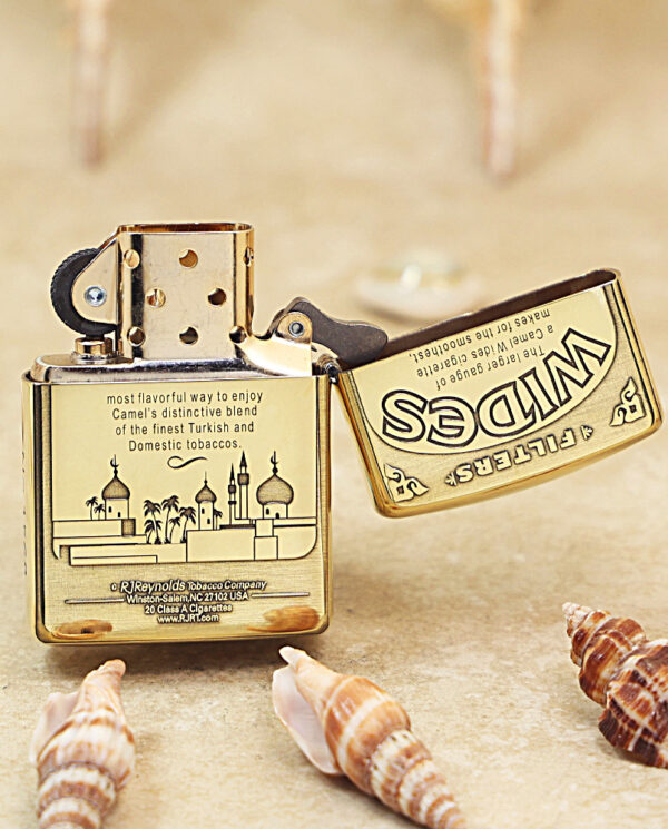 KZ242-03 Gold Zippo lighter with an engraving of a skyline on a beige surface, lid open, surrounded by seashells.