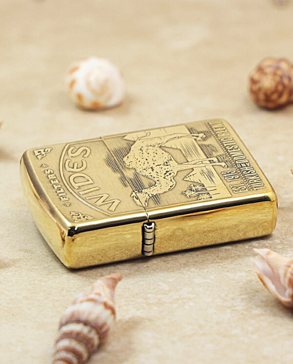 KZ242-04 Gold-tone Zippo lighter with engraved map on lid, resting on sandy surface among seashells
