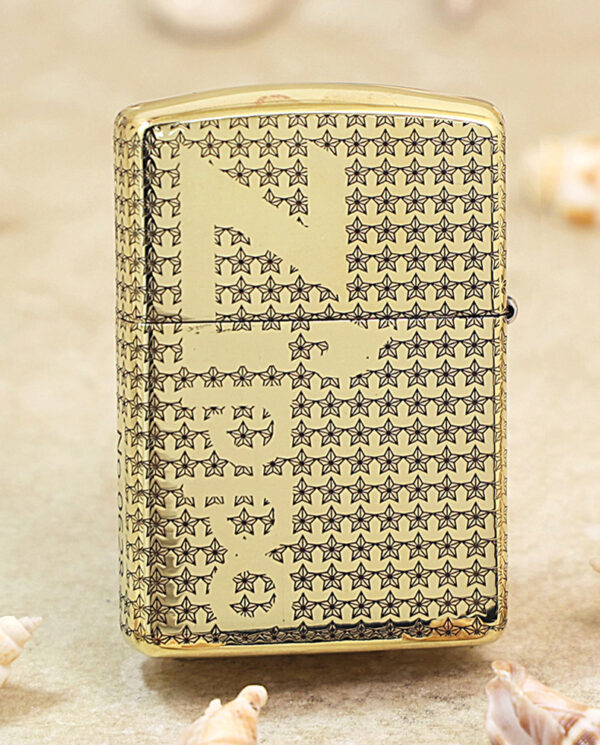 Gold Zippo lighter with a repeating star pattern on a sandy beach with seashells nearby.