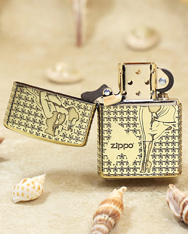 Gold Zippo lighter with star-pattern and silhouettes, lid open, resting on sand with seashells in the foreground and background.