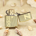 Gold patterned lighter on sand with its lid open, surrounded by seashells on a beach.