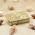 Gold Zippo-style lighter with a star pattern resting on a sandy surface among seashells.