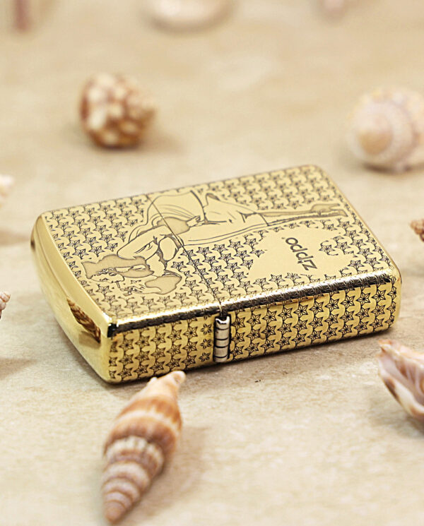 Gold Zippo-style lighter with a star pattern resting on a sandy surface among seashells.