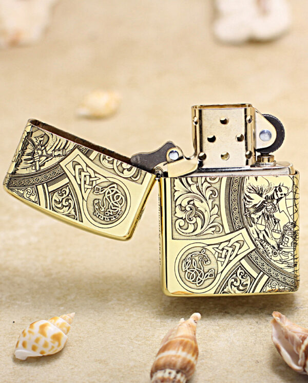 KZ245-02 Gold engraved Zippo-style lighter open on a sandy beach with scattered seashells nearby, intricate patterns visible on the metal.