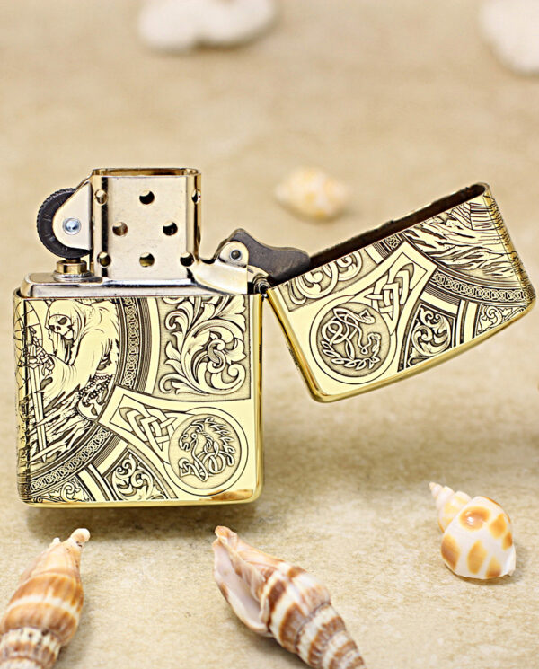 KZ245-03 Gold ornate lighter on its side with lid open, placed on sand among seashells; decorative engravings visible on the metal surface.
