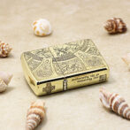 Gold ornate lighter with intricate engravings on a sandy beach, surrounded by seashells