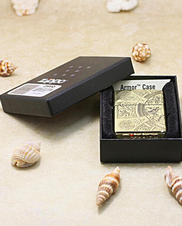 KZ245-06 Ornate metal lighter in an open black box labeled Armor Case, surrounded by small seashells on a sandy surface.