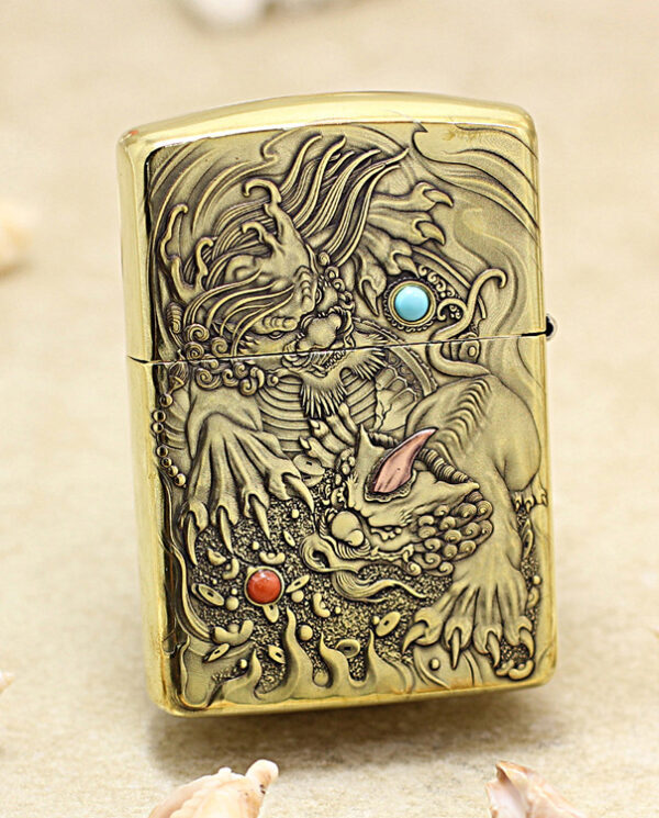 Metal lighter with an ornate dragon relief and colored stone inlays on a sandy beach backdrop.