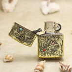 Gold engraved dragon lighter open to reveal ornate designs, resting on sandy beach with seashells nearby