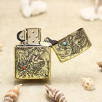 Gold-tone lighter with dragon relief engraving on a sandy beach, lid open among seashells