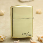 Gold Zippo-style lighter with numbered edition 223/500 on a sandy background with small seashells nearby