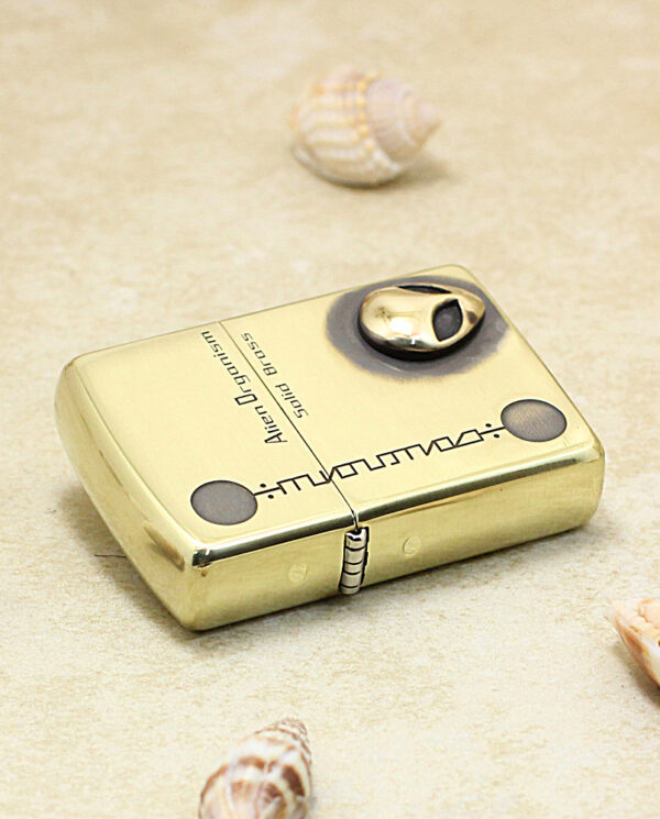 KZ253-04 Gold Zippo-style lighter lying on sand with seashells scattered around it, decorative and beachy.
