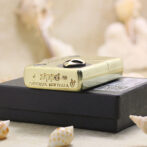 Gold Zippo lighter with Bradford, PA made in USA engraving resting on a black box, surrounded by seashells.