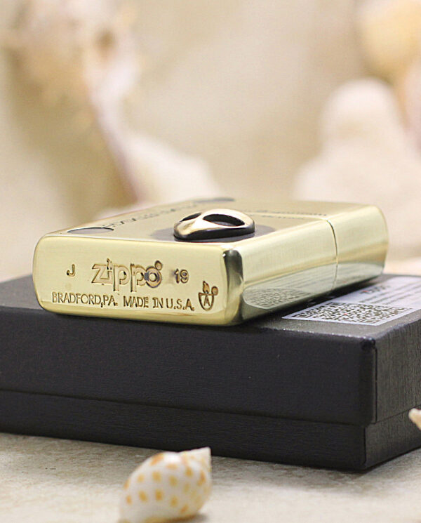 KZ253-05 Gold Zippo lighter with Bradford, PA made in USA engraving resting on a black box, surrounded by seashells.