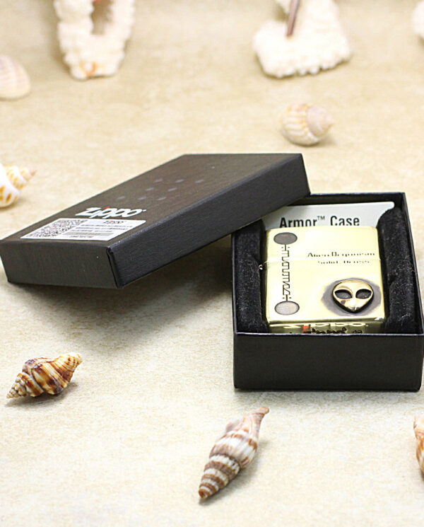 KZ253-06 A small metal lighter in an open black box on a sandy surface with seashells scattered around.
