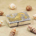 Metal lighter with gold dragon engraving on a silver body, resting on sand among seashells.