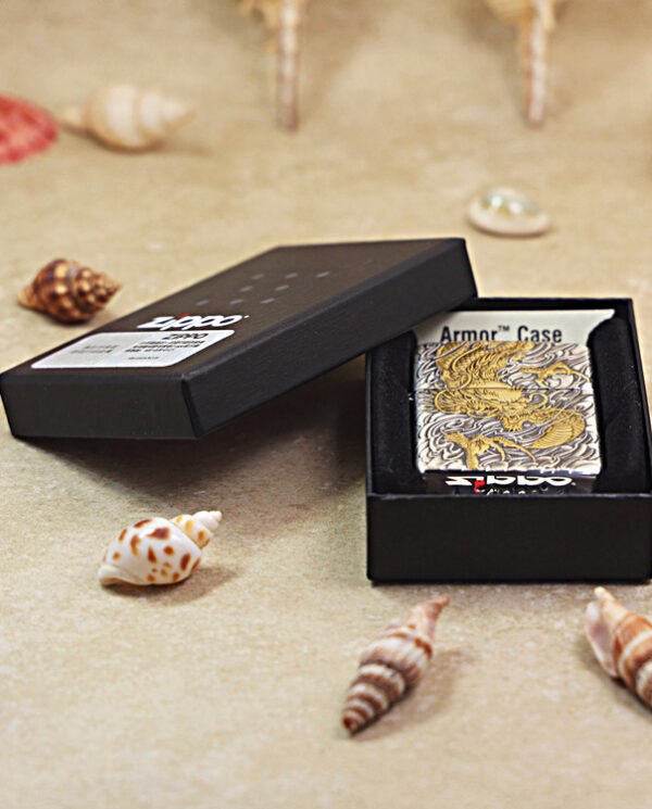 KZ282-06 Open black box reveals a silver metal case with a gold dragon design on a sandy surface with seashells nearby.