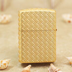Gold woven-pattern lighter standing upright on a sandy surface with seashells around.