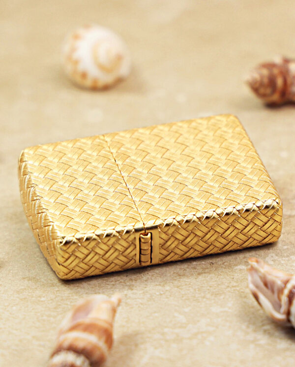 KZ284-04 Gold woven jewelry box resting on sandy surface with seashells around it on a beach-like setting.
