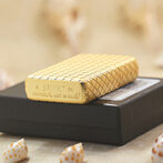 Woven straw Zippo lighter resting on a black box, with blurred beige background and small seashells nearby.