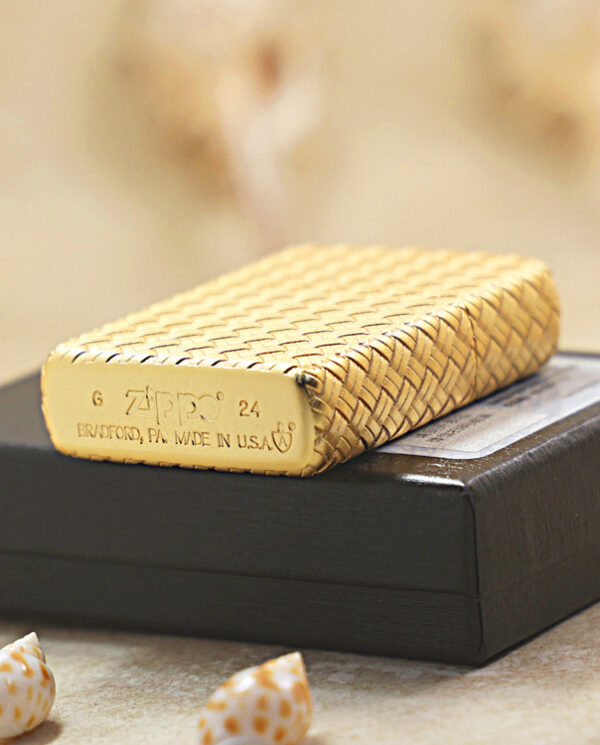 KZ284-05 Woven straw Zippo lighter resting on a black box, with blurred beige background and small seashells nearby.