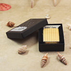 Gold textured Zippo lighter in a black box labeled Armor Case on a sandy beach with seashells.
