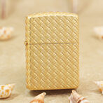 Gold woven-pattern lighter standing on sand with small seashells around it.