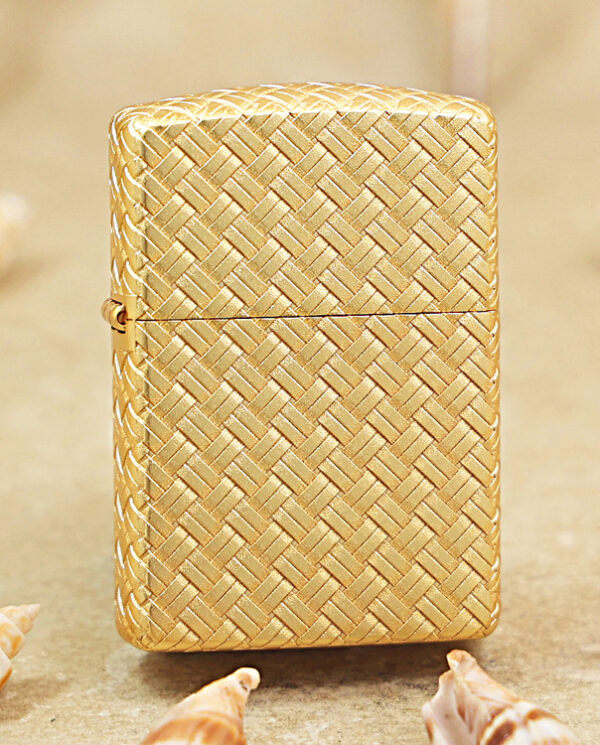 KZ284 Gold woven-pattern lighter standing on sand with small seashells around it.