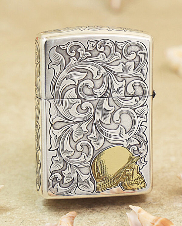 KZ286-01 Engraved silver lighter with intricate swirling floral pattern and a gold skull at the lower corner.