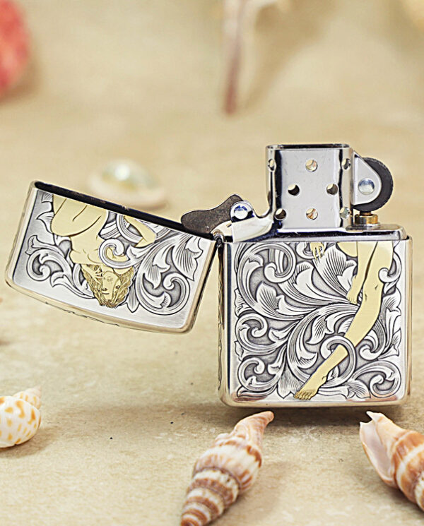 KZ286-02 Open silver lighter with ornate scrollwork and a cream ribbon motif, set on sandy beach with seashells.