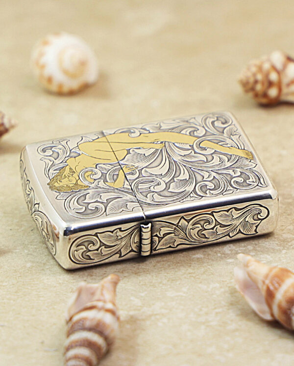 KZ286-04 Ornate metal lighter with intricate floral engravings and a gold fish motif, set on a sandy surface with seashells nearby