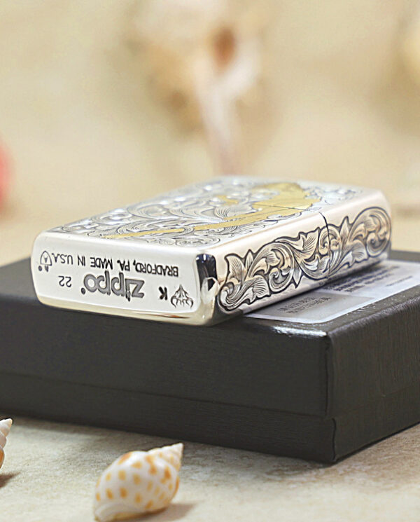 KZ286-05 Engraved silver Zippo lighter with a floral pattern resting on a black box, with small seashells in the foreground.