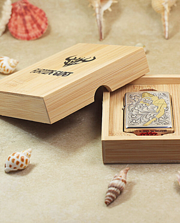 KZ286-06 Open wooden gift box reveals a decorative metal lighter with floral engraving on a sandy surface with seashells nearby.