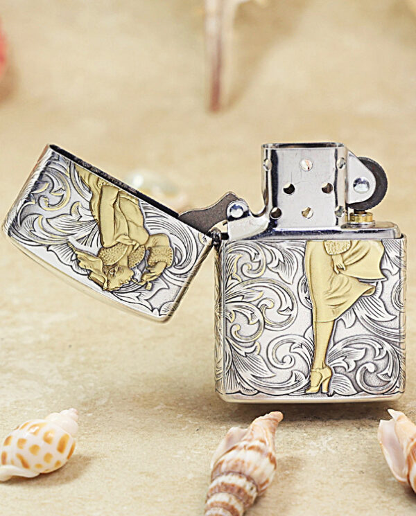 KZ287-02 Engraved metal lighter with floral scrolls and a gold-dressed woman, lid open on a sandy surface.