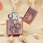 Copper-toned Zippo lighter with an open lid, featuring an engraved hand holding a lotus flower on the body.