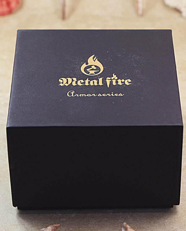 KZ288-06 Black box with a gold embossed logo and the words 'Metal Fire' and 'Armor Series' on the lid, placed on a light surface with small shells around.