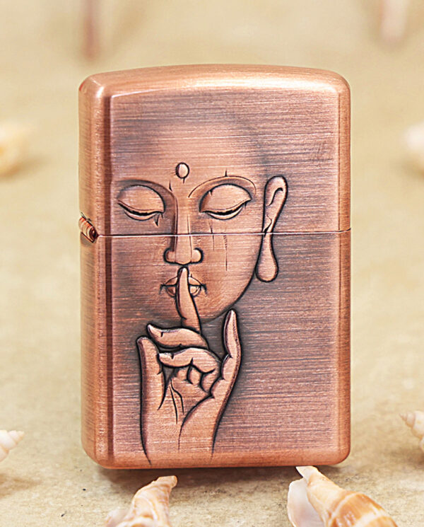KZ288 Copper-colored lighter engraved with a calm face making a shushing gesture (finger to lips); shells in a sandy background.