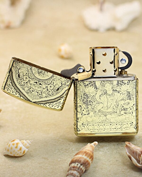 KZ304-02 Gold engraved lighter with open lid on a sandy beach among seashells.