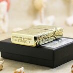 Ornately engraved metal lighter resting on a black gift box, with small seashells in the foreground.