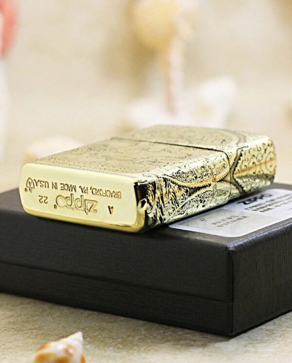 KZ304-05 Ornately engraved metal lighter resting on a black gift box, with small seashells in the foreground.