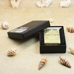 Ornate gold lighter in a black box on a sandy surface with seashells around.