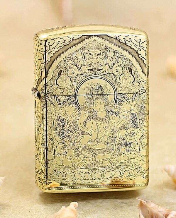 KZ304 Gold Zippo-style lighter with an intricate Buddhist deity engraving and floral patterns on a sandy surface.