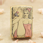 Gold-colored lighter with a pin-up style illustration of a woman in a pink dress seated with legs raised, set against a curtained backdrop on the lid and body.