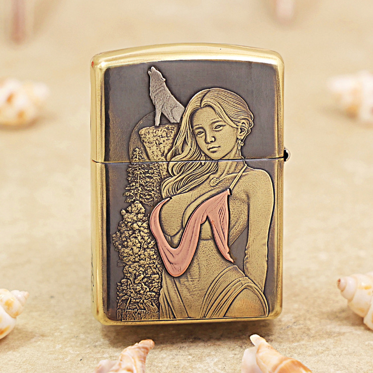 Brass Zippo-style lighter with an engraved panel showing a woman in a pink bikini top beside a forest scene, set on a sandy background with seashells nearby.