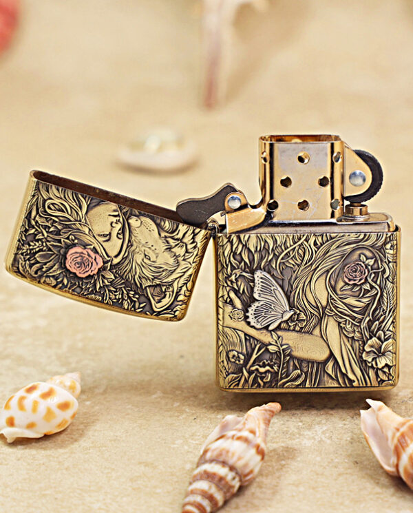 KZ452-02 Ornate brass lighter with intricate floral engravings and a butterfly design, lid open on a sandy surface with shells nearby.
