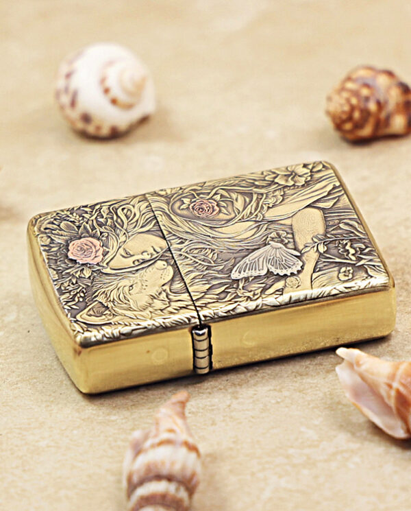 KZ452-04 Brass Zippo-style lighter with intricate floral and moth engravings resting on sand among seashells.