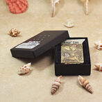 Open black gift box revealing a decorative Zippo lighter with an intricate floral engraving, labeled 'Armor Case' on a sandy, seashell-strewn surface