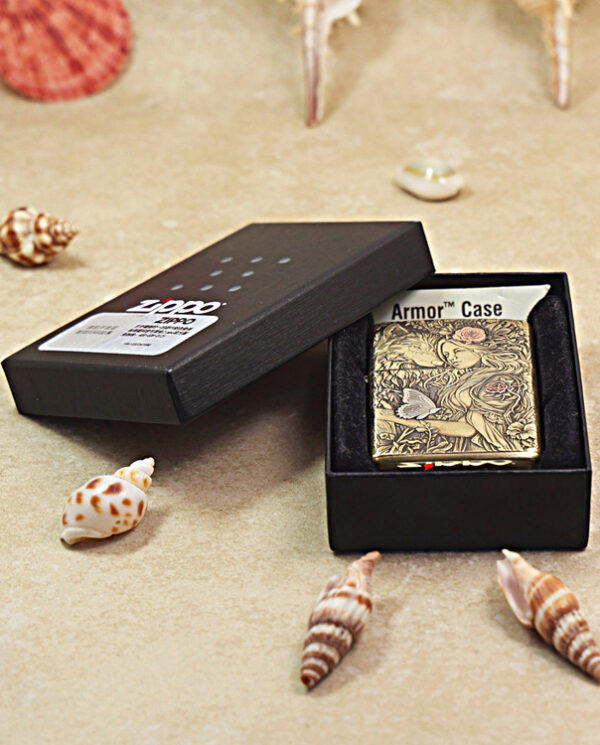 KZ452-06 Open black gift box revealing a decorative Zippo lighter with an intricate floral engraving, labeled 'Armor Case' on a sandy, seashell-strewn surface
